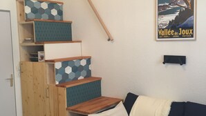 A staircase with wooden steps and geometric-patterned cushions, a dark blue sofa with a white cushion, and a poster of a mountain scene.