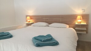 A neatly made bed with white bedding and two folded towels. There are two bedside tables with lamps and a wooden headboard.