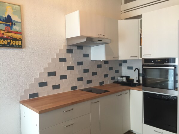 Una cocina moderna con armarios blancos, encimera de madera, horno empotrado y salpicadero azulejado.