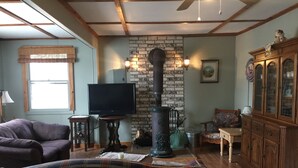 A cozy living room with a plaid sofa, a television on a wooden stand, a brick wall, and a wooden cabinet. - house with beach and dock access (Willsboro)
