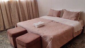 A neatly made bed with a pink bedspread and matching pillows, a white towel on the bed, and two pink ottomans. - Tasumuka Savaal (Johannesburg)