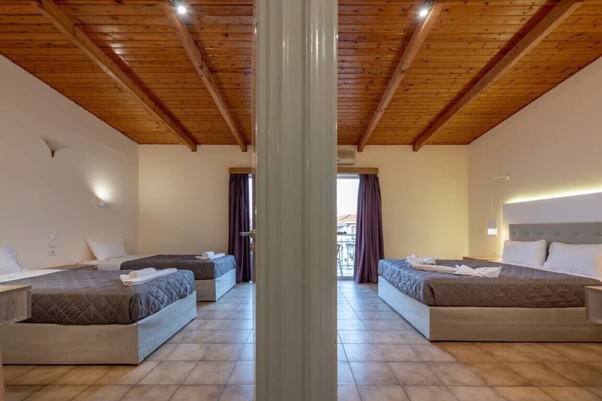 A hotel room with two beds, wooden ceiling beams, and a view through a doorway.