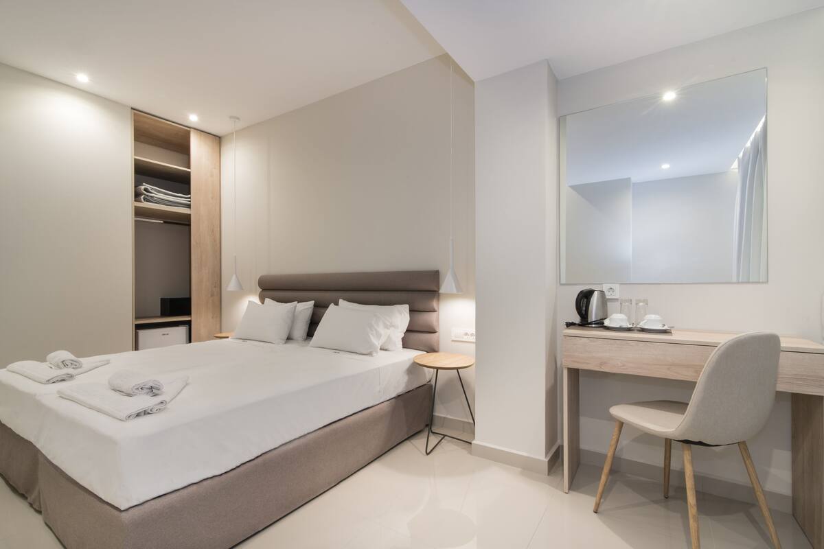 A modern hotel room with a large bed, a desk, and a wardrobe.