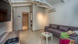 Un salon moderne avec un canapé, une petite table et un téléviseur. Un couloir mène à une autre pièce.