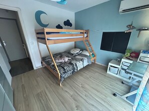Un lit superposé avec une échelle, un bureau avec des tiroirs de rangement, une horloge murale et un ventilateur de plafond.