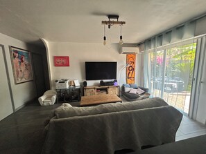A modern living room with a sofa, a flat-screen TV, a coffee table, and a large window with a view of the outside.