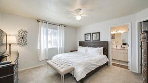 Un dormitorio con cama, ventilador de techo, cómoda, tocador con espejo y ventana con cortinas.
