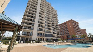Un hotel de varios pisos con piscina, mobiliario exterior y cielo despejado.