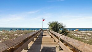 Un paseo marítimo de madera que conduce a la playa, con sombrillas y una bandera.