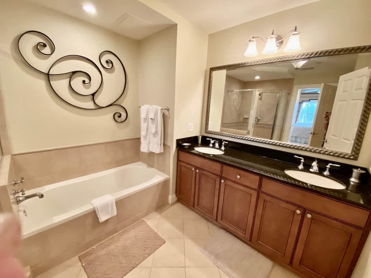 Un baño con bañera, dos lavamanos, un espejo grande y un adorno en la pared.
