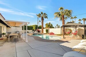 Un jardin avec une piscine, un espace salon extérieur, des palmiers et une pergola.