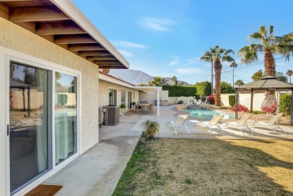 Une maison moderne dotée d’un patio couvert, d’une piscine et de chaises longues.