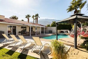 Un espace piscine avec des chaises longues, un coin salon abrité et un toboggan.
