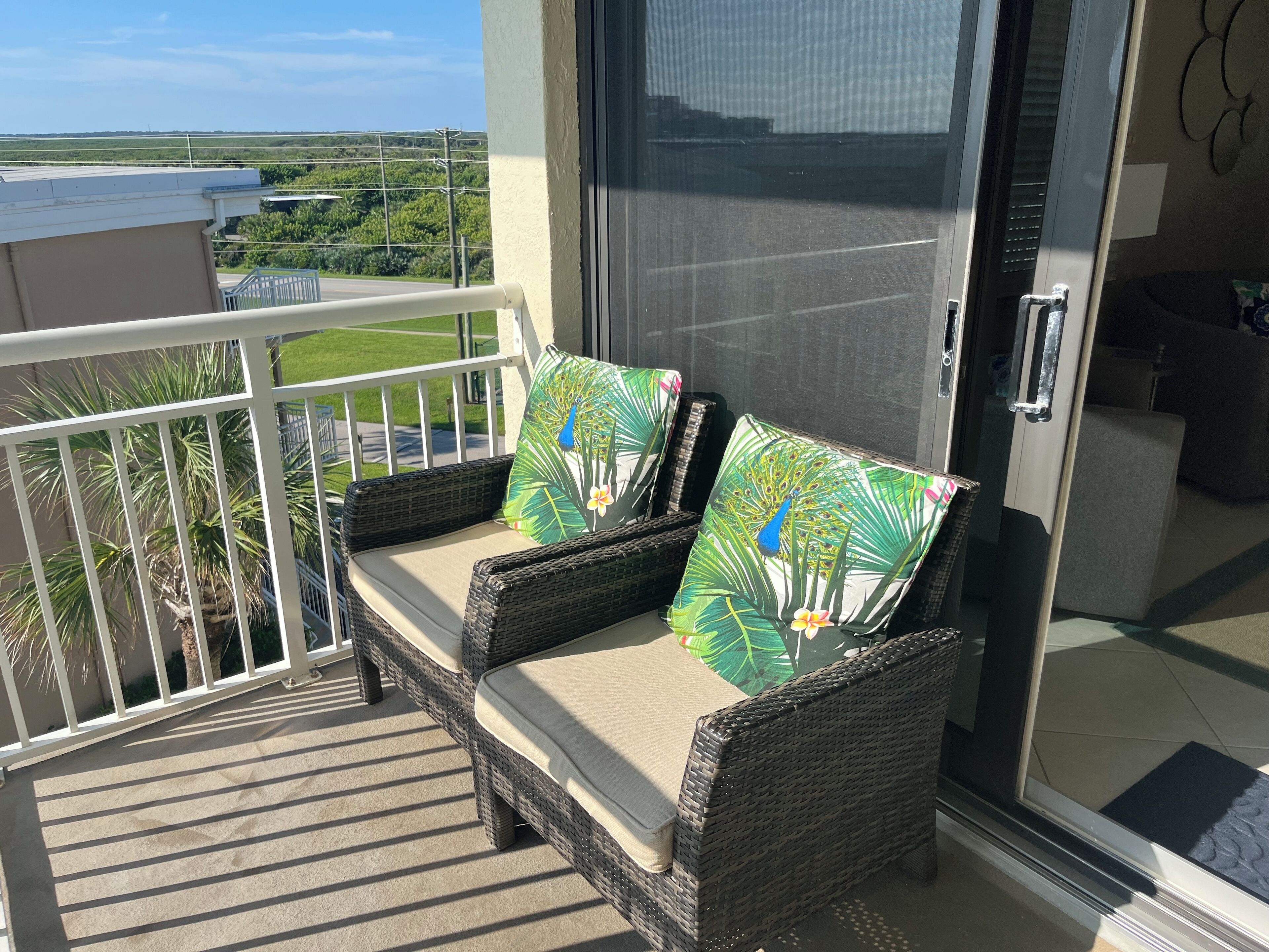 A balcony with wicker furniture, including two chairs with cushions and a small table.