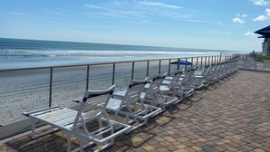 En strandpromenade med hvide liggestole og en blå parasol.