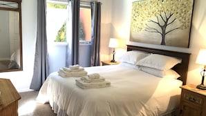 A neatly made bed with white linens, a bedside lamp, and a painting of a tree on the wall. - LAKESHORE VILLAS BEACH COWBOY VILLA (Osoyoos)