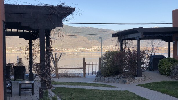 A patio area with outdoor seating, a view of a lake, and a distant cityscape. - LAKESHORE VILLAS BEACH COWBOY VILLA (Osoyoos)