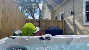 Een hottub met stromend water, omgeven door een houten omheining, een groot blad en een barbecue.