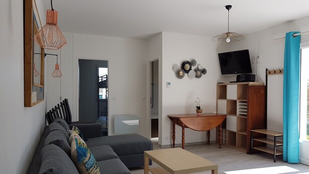 Una sala de estar moderna con un sofá gris, una mesa de centro de madera y un televisor sobre un mueble de madera.