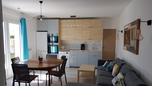 Una cocina moderna con armarios de madera, un área de comedor con mesa y sillas de madera, y un sofá gris con una manta de colores.