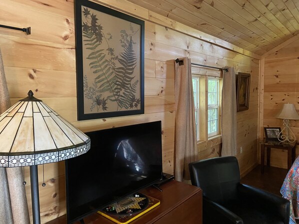 Un interior de madera con televisor, una impresión enmarcadas de motivos botánicos y una ventana con cortinas.