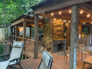 Una terraza de madera con mobiliario exterior, una chimenea de piedra y luces colgantes.
