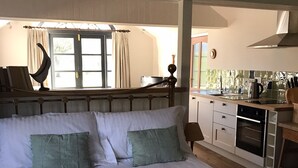 A bedroom with a large bed, a view of the kitchen, and a window with curtains.