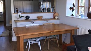 A spacious kitchen with a wooden table and chairs, a window with a view, and a dining area with a black sofa.
