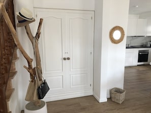 Een witte deur met twee handgrepen, een houten trap met een leuning, en een keuken met witte kasten en een zwarte oven.