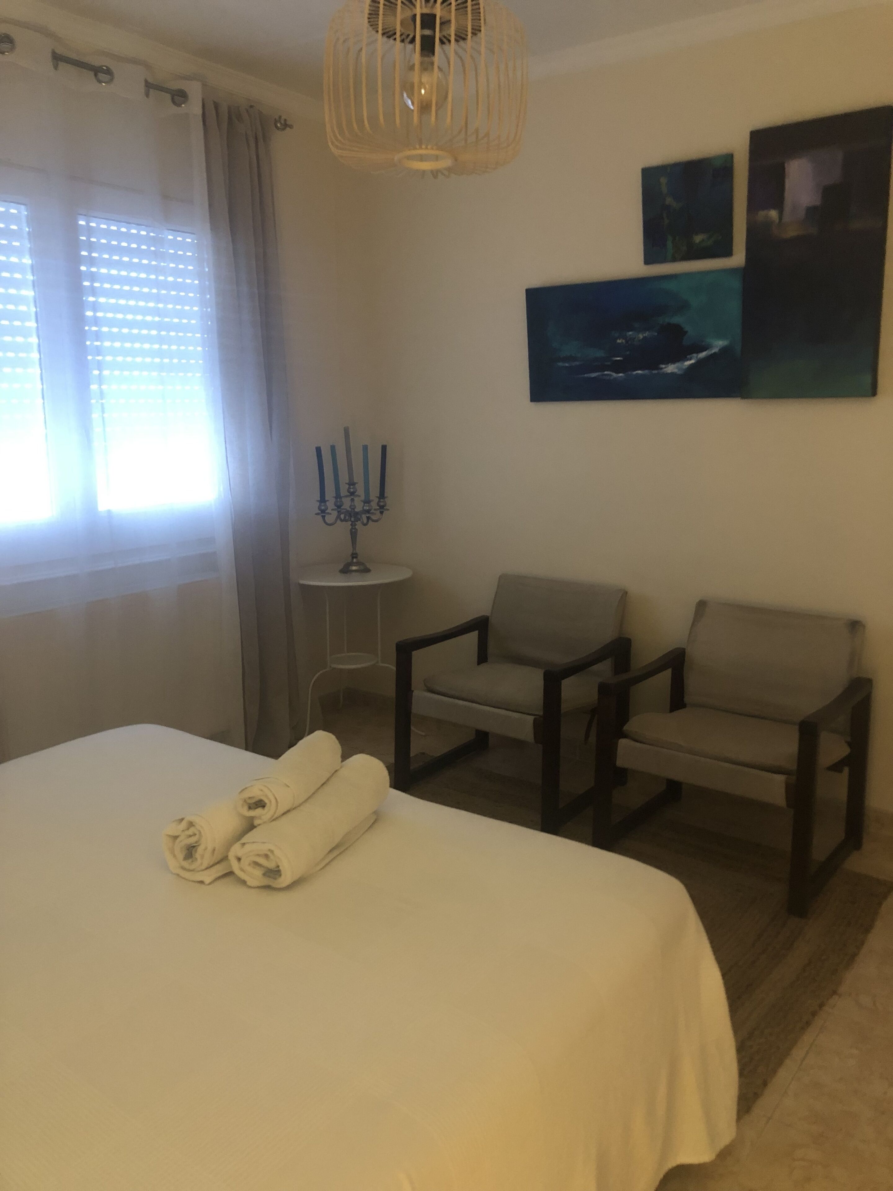 A hotel room with a bed, two armchairs, a small table with a candelabra, and artwork on the wall.
