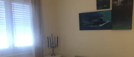 A hotel room with a bed, two armchairs, a small table with a candelabra, and artwork on the wall.