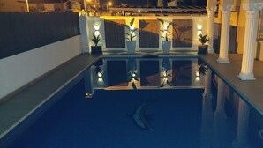 A pool area with a dolphin sculpture, white columns, and potted plants. - Modern 4-bedroom villa, private pool, near beach.  (Empuriabrava)