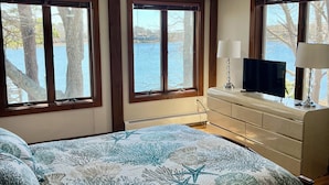 Un dormitori amb un llit, un ambell, una televisió i finestres amb vista a un cos d'aigua.