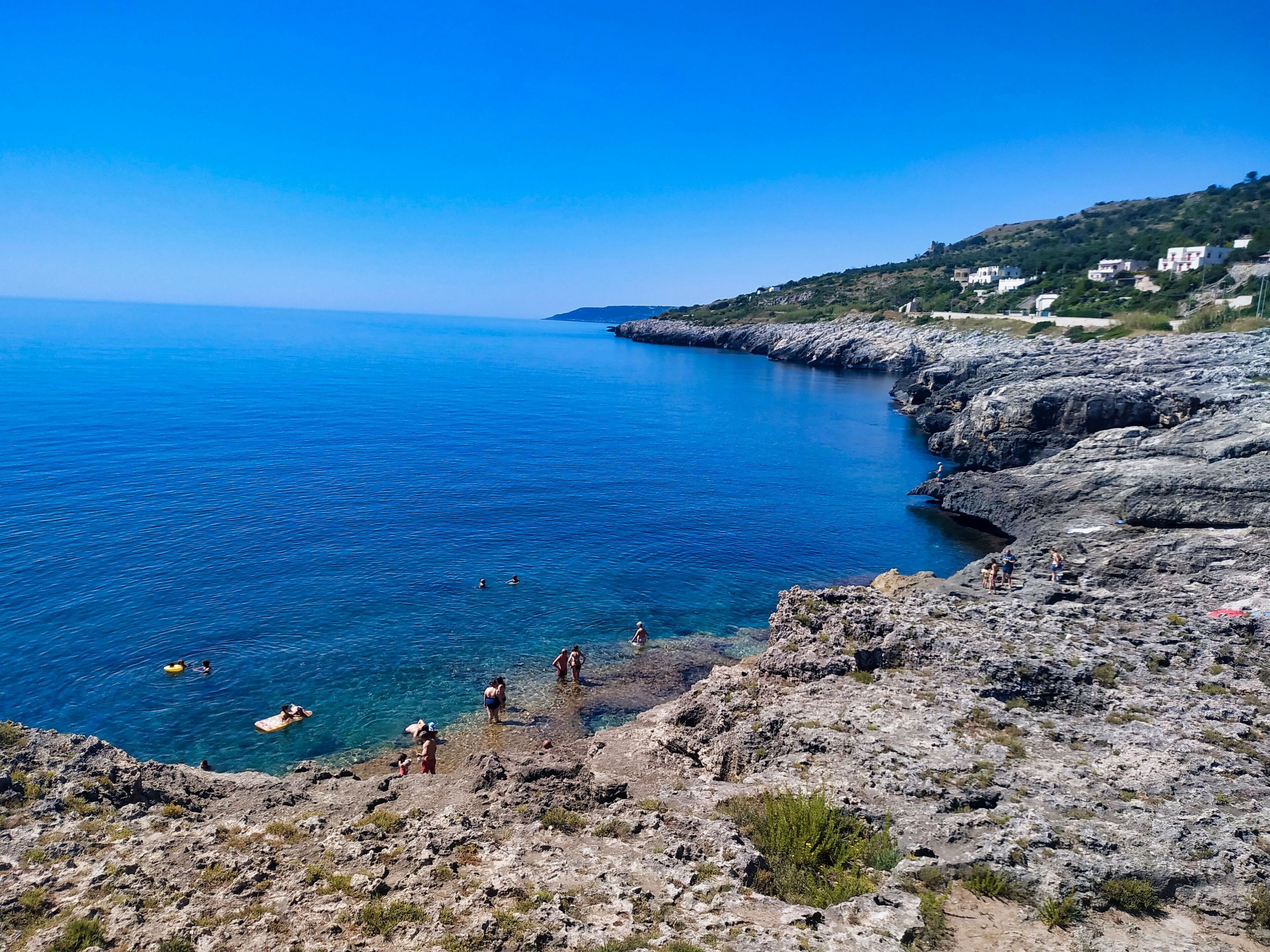 Paesaggio costiero con terreno roccioso e mare blu limpido.