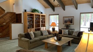 A spacious living room with a high ceiling, built-in wooden bookshelves, a large window with a view of trees, and a cozy seating area with a coffee table. - SM BBR home - Perfect for two families! (Sisters)