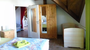 A bedroom with a wooden ceiling, a bed with a floral bedspread, a green chair, and a wooden wardrobe. - Holiday apartment / accommodation for business travelers (Sandberg)