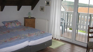 A bedroom with a bed, a nightstand, a lamp, a window with a view of the outside, and a balcony with a chair. - Holiday apartment / accommodation for business travelers (Sandberg)