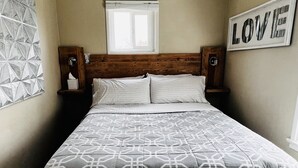 A bedroom with a geometric patterned bedspread, a wooden headboard, bedside tables, and a wall-mounted sign that reads "LOVE". - Central Coast Cottage (Arroyo Grande)