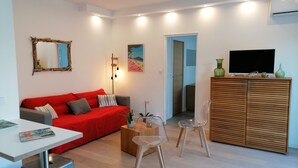A modern living room with a red sofa, a wooden cabinet, and a TV. - A 200 m des Plages Appartement Avec Terrasse & Jardin (Saint-Cyr-sur-Mer)
