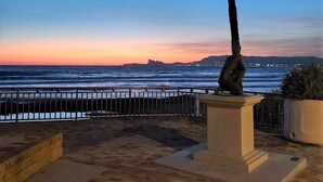 A coastal promenade with a palm tree and a statue, leading to a beach with a clear view of the ocean and distant city lights. - A 200 m des Plages Appartement Avec Terrasse & Jardin (Saint-Cyr-sur-Mer)