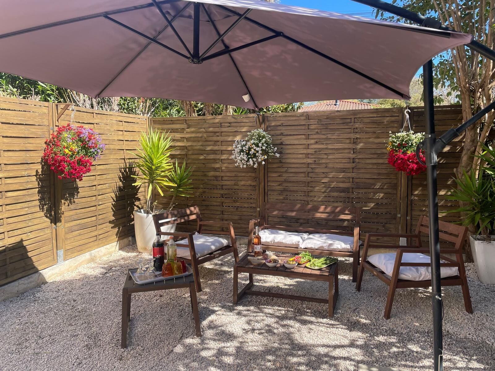 Eine Terrasse mit Holzzaun, zwei Holzstühlen, einem Tisch mit Speisen und einem großen Sonnenschirm.