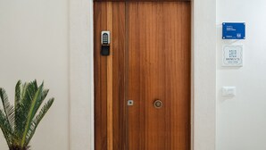 Una puerta de madera con cerradura electrónica, una planta en maceta y dos letreros en la pared que indican el número de habitación y una calificación.