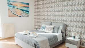 Un dormitorio moderno con una cama, mesitas de noche, un radiador y un papel tapiz estampado.