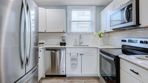 A modern kitchen with stainless steel appliances, white cabinetry, a dishwasher, and a window with blinds. - Steps to Rehoboth Beach and Boardwalk Dog Permitted (Rehoboth Beach)