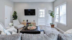 A living room with a sofa, a coffee table, a TV, and a door. - Steps to Rehoboth Beach and Boardwalk Dog Permitted (Rehoboth Beach)