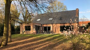 Et murstenshus med skråt tag, store vinduer og en terrasse.