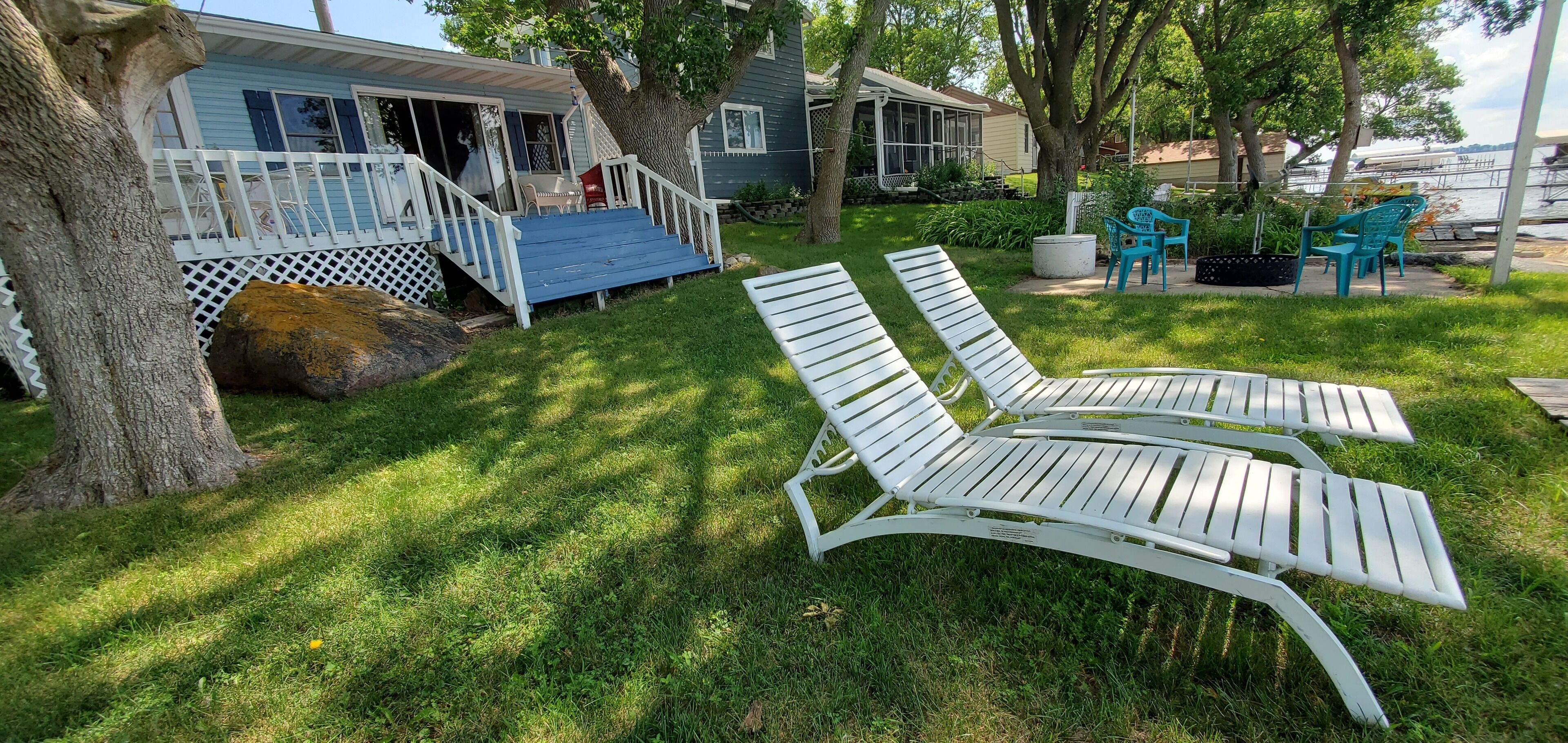 Een achtertuin met twee witte loungestoelen, een overdekt terras en een huis met een veranda.
