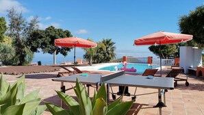 Ein Poolbereich mit zwei Tischtennisplatten, roten Sonnenschirmen und einem Flamingo-Schwimmpunkt.