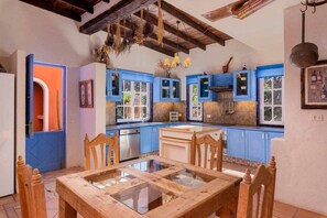Une cuisine avec des meubles de rangement bleus, une table à manger en bois et un luminaire suspendu.