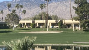 A golf course with a pool, palm trees, and mountain views in the background.